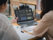 Two businesspeople or an accountant team are analyzing data charts, graphs, and a dashboard on a laptop screen in order to prepare a statistical report and discuss financial data in an office.